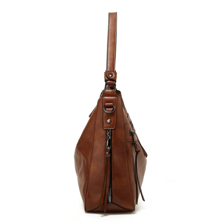 A soft brown vintage shoulder bag with zip pockets and tassel pulls, carried on the shoulder in town.
