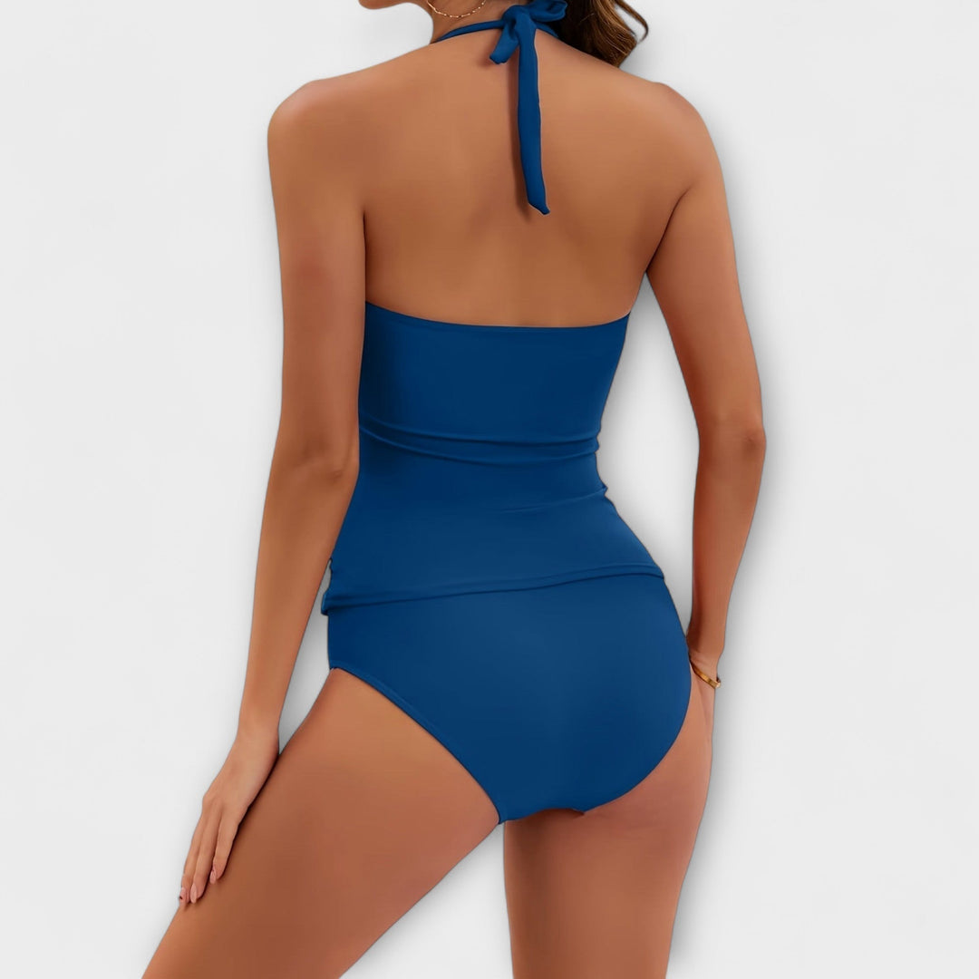A woman by the water in a solid-colour two-piece halter swimsuit, relaxed and confident in the sun.
