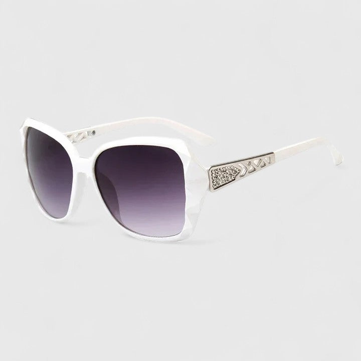 A woman on a sunny city street wearing chic square-frame sunglasses, smiling confidently.