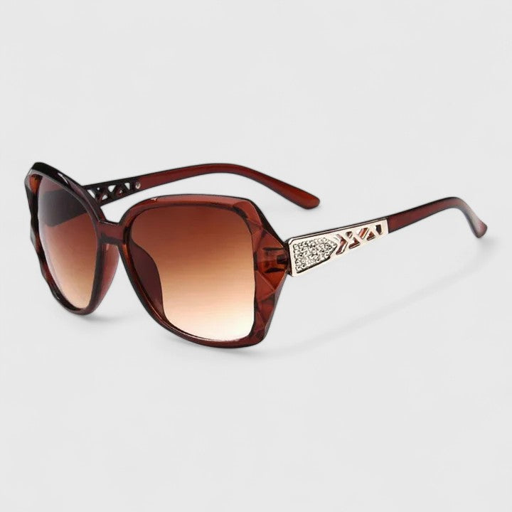 A woman on a sunny city street wearing chic square-frame sunglasses, smiling confidently.