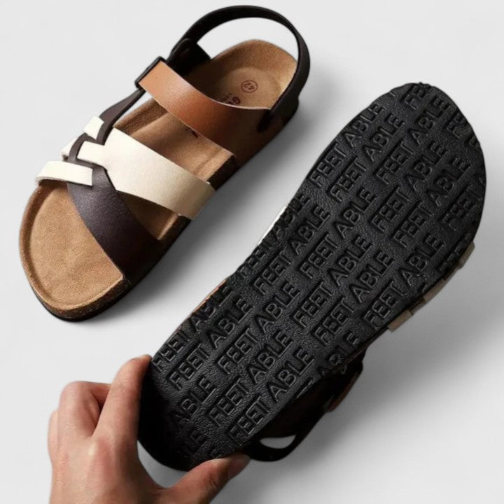 A woman wearing cream and brown multi-strap supportive sandals, standing steady and relaxed on a sunny path.