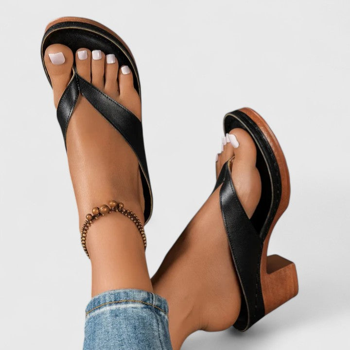 A woman in black open toe-post sandals with a chunky squared heel, walking easily through an evening event.