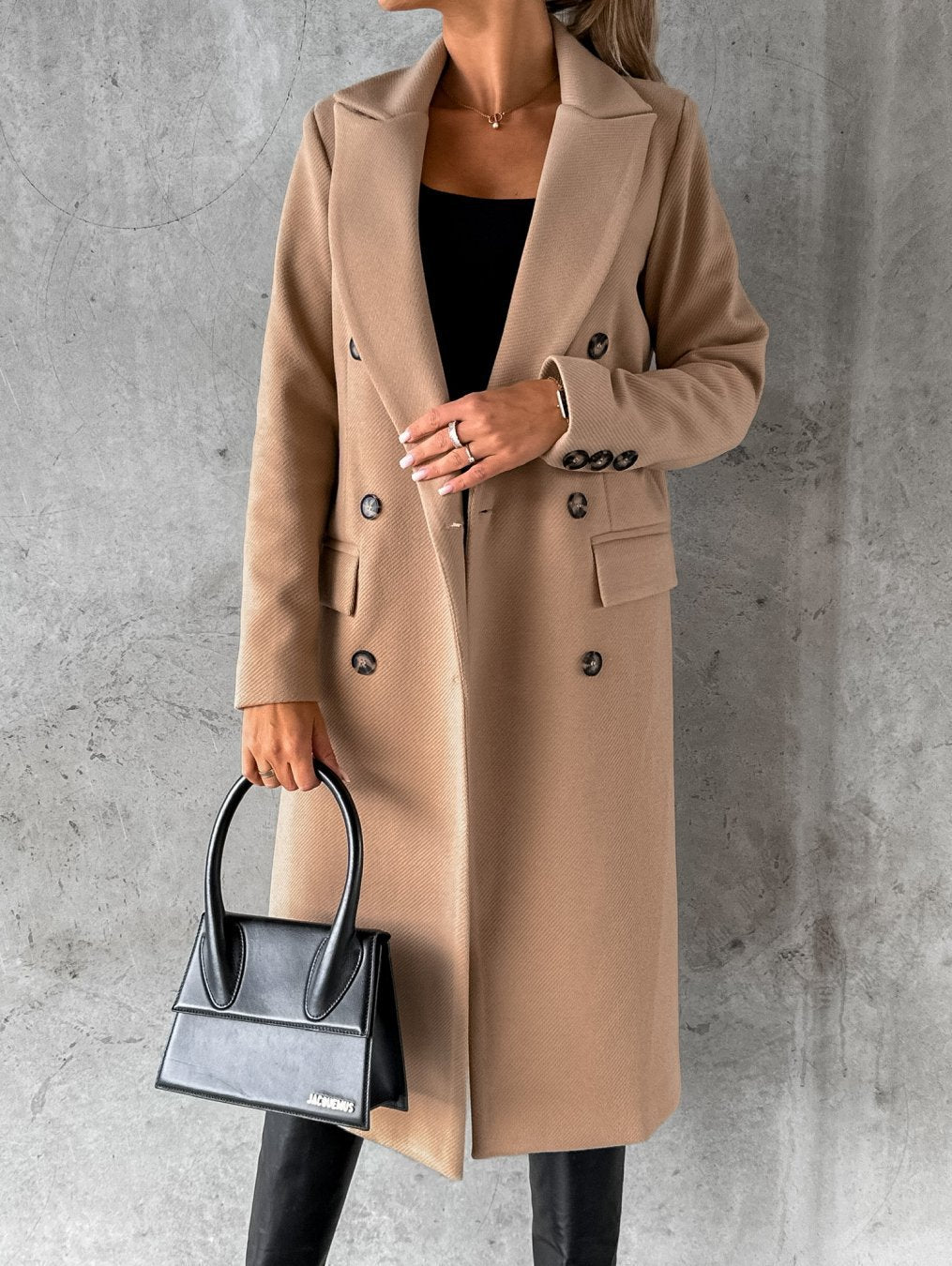A woman wearing a long waisted coat, standing elegantly outdoors