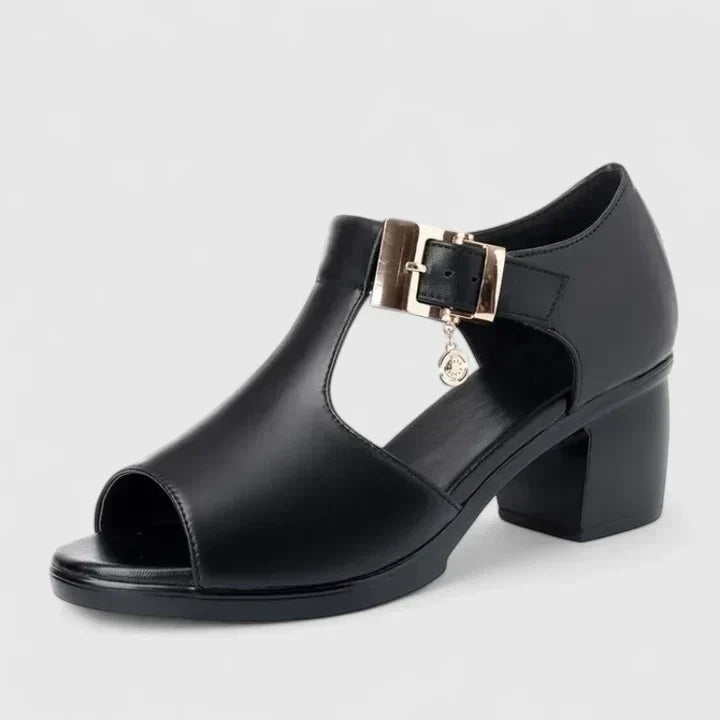 A woman wearing black peep-toe block heels with a T-strap and gold buckle.