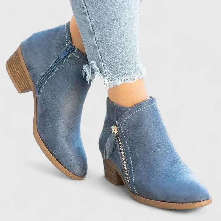 Woman wearing black side-zip ankle boots, stepping off a kerb in town.