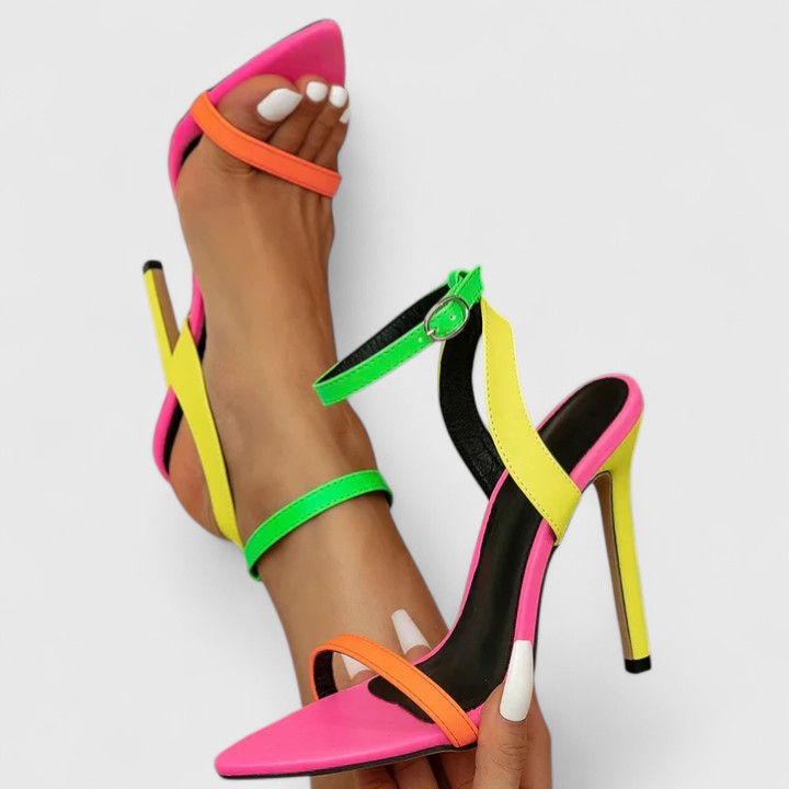 A woman wearing bright neon multicolour stiletto pumps with a slim heel and ankle strap.