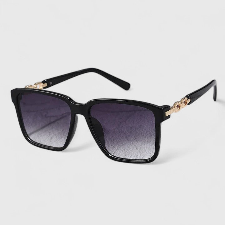 A woman by the pool wearing bold square sunglasses with chain-detail temples, confident in the sun.