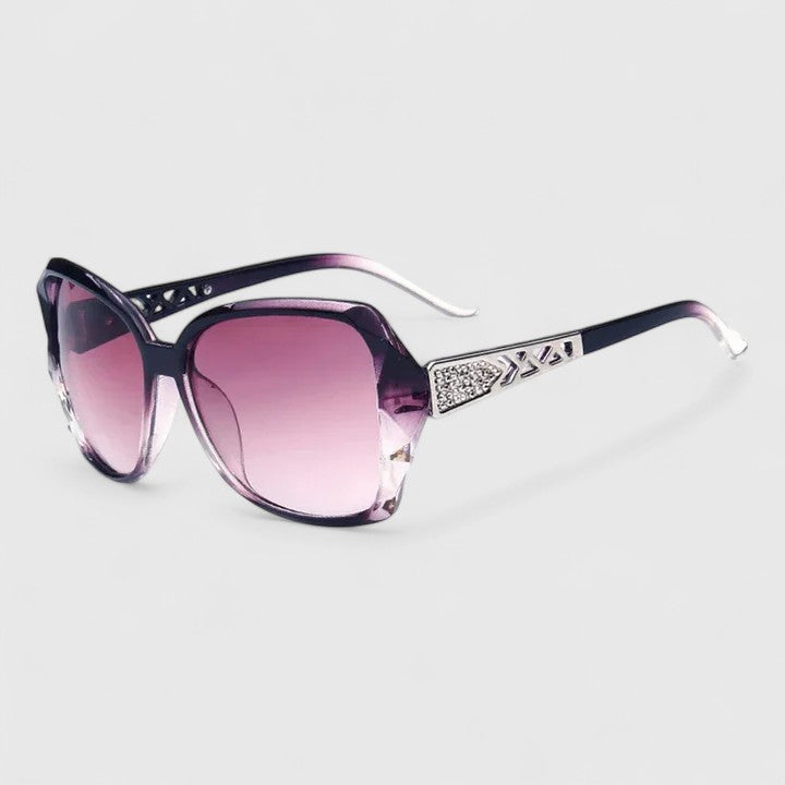 A woman on a sunny city street wearing chic square-frame sunglasses, smiling confidently.