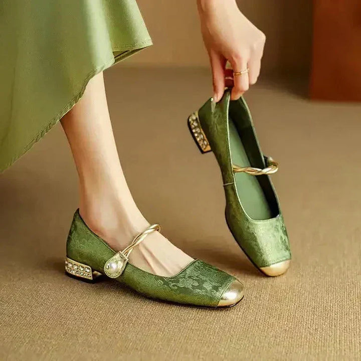 A woman wearing green low-heel Mary Janes with a twisted gold strap, gilded cap toe and a crystal-set heel