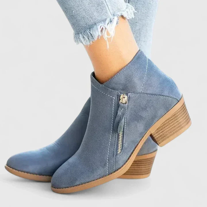 Woman wearing black side-zip ankle boots, stepping off a kerb in town.