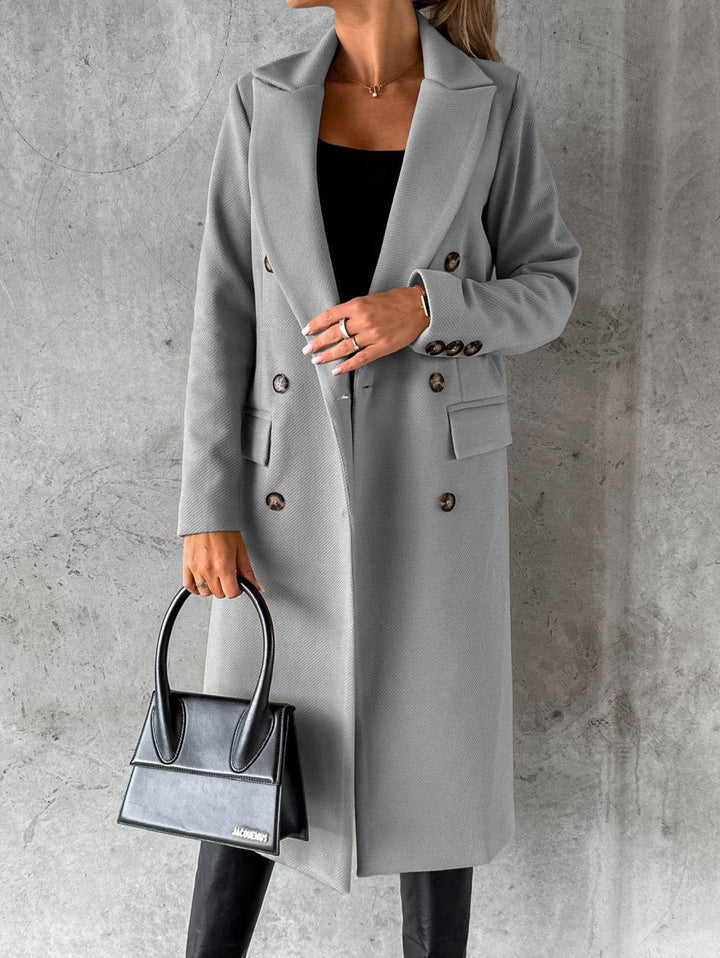 A woman wearing a long waisted coat, standing elegantly outdoors