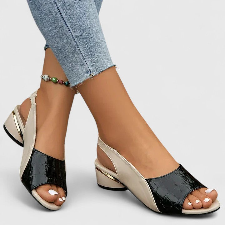 A woman wearing two-tone low-heel dress sandals with an adjustable heel strap at a summer occasion.