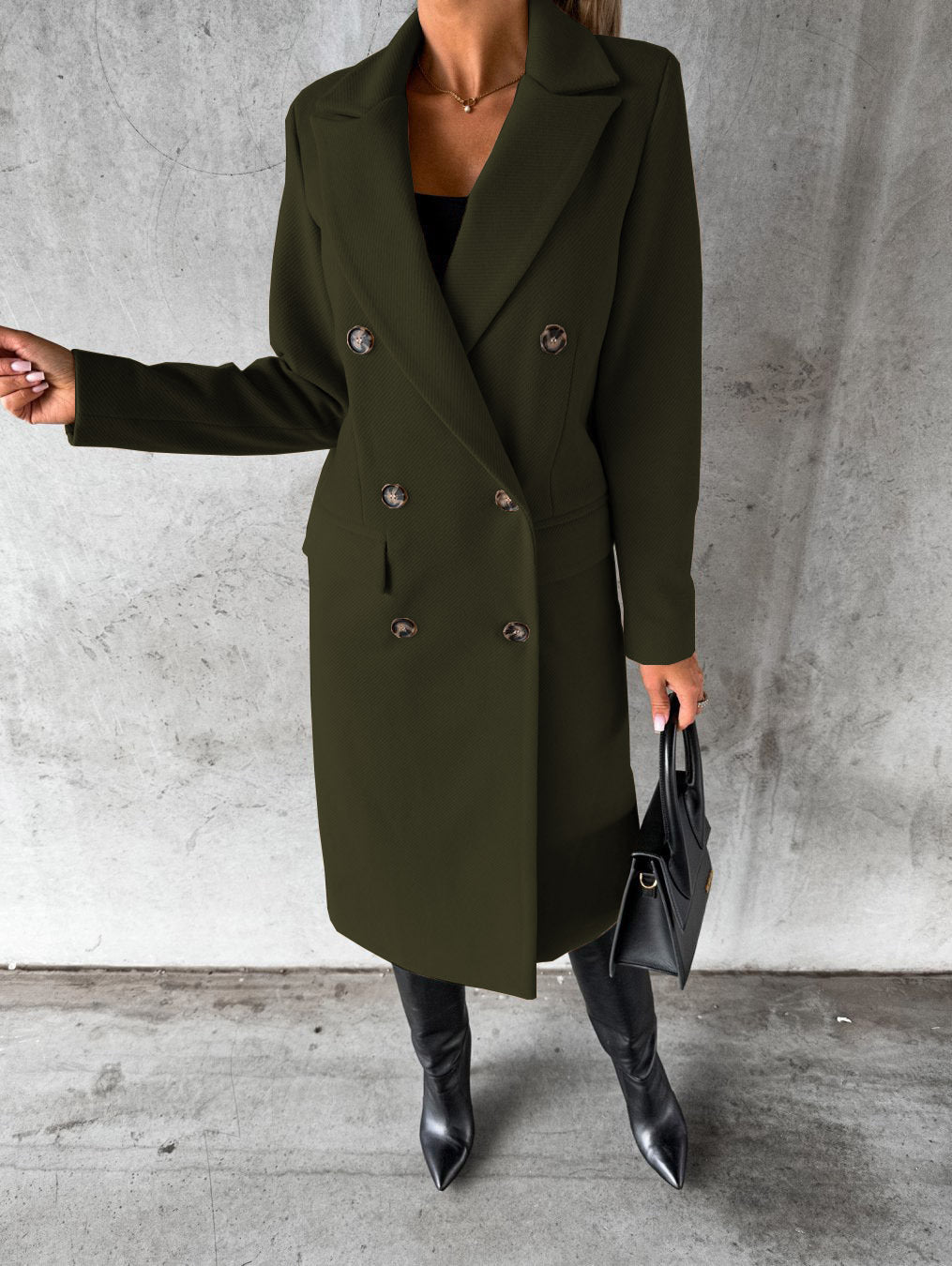 A woman wearing a long waisted coat, standing elegantly outdoors