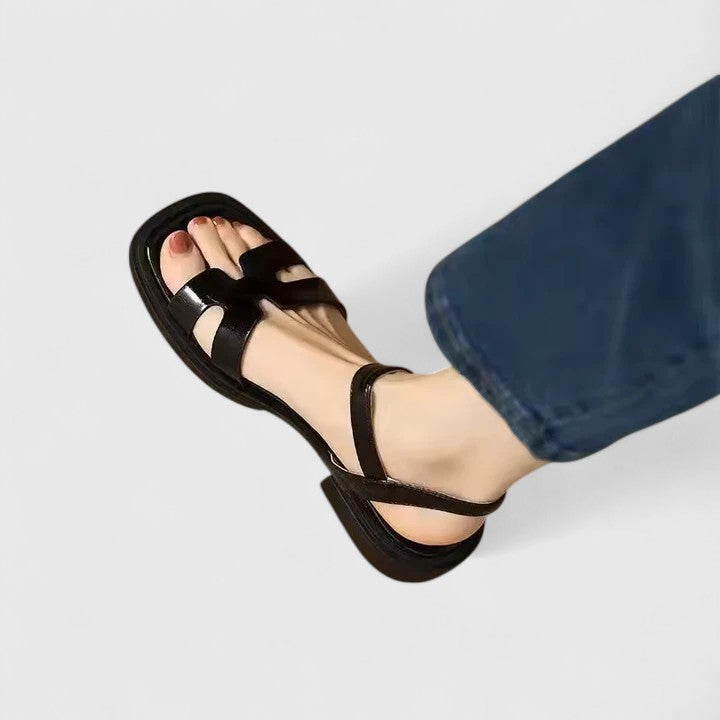 A woman wearing minimalist black strappy sandals with a summer dress, looking chic and at ease.