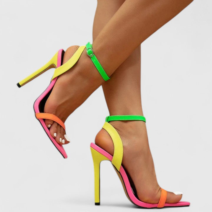 A woman wearing bright neon multicolour stiletto pumps with a slim heel and ankle strap.