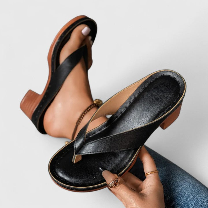 A woman in black open toe-post sandals with a chunky squared heel, walking easily through an evening event.