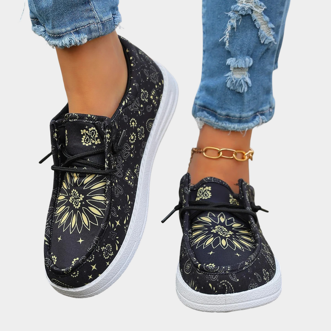 A woman wearing bold black and yellow boho-print lace-up comfort shoes on a bright day.