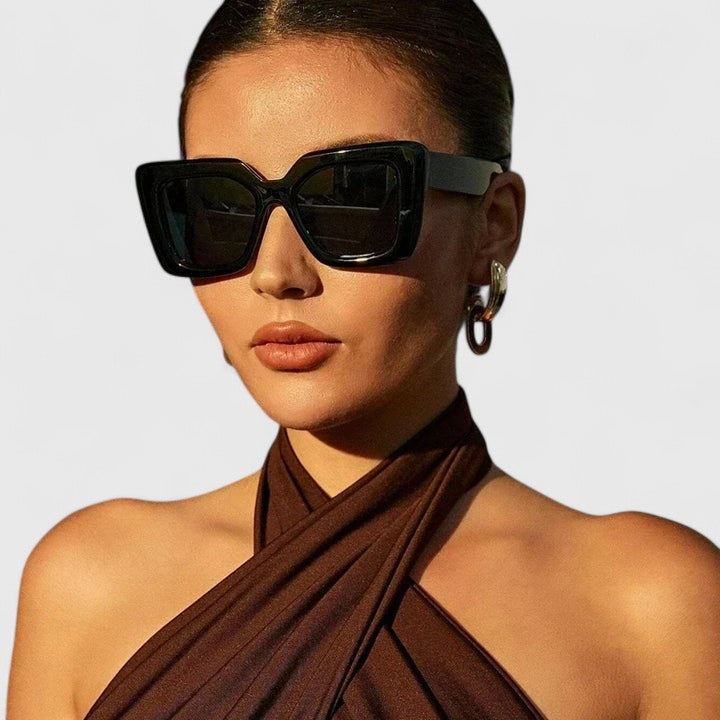 A woman at golden hour wearing bold geometric sunglasses, poised and glamorous in the sun.