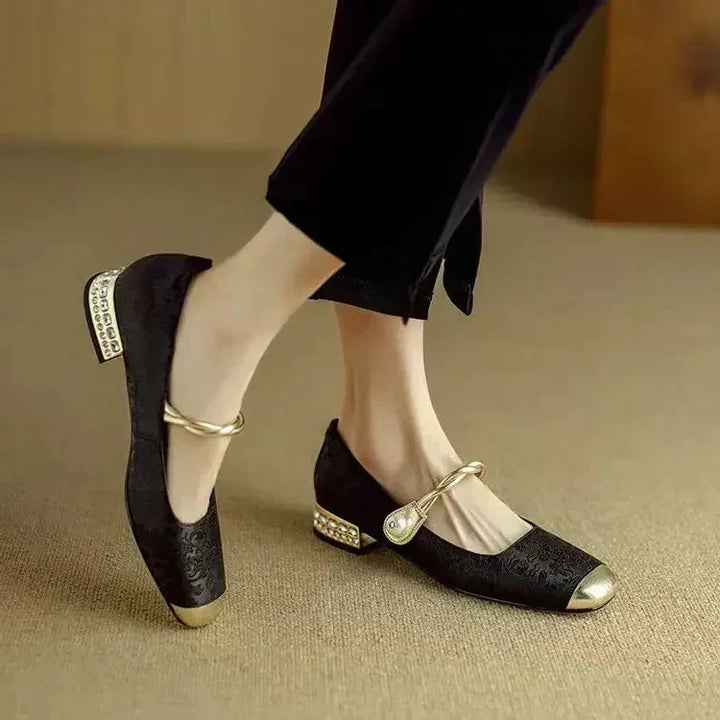 A woman wearing green low-heel Mary Janes with a twisted gold strap, gilded cap toe and a crystal-set heel