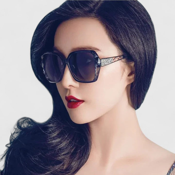 A woman on a sunny city street wearing chic square-frame sunglasses, smiling confidently.