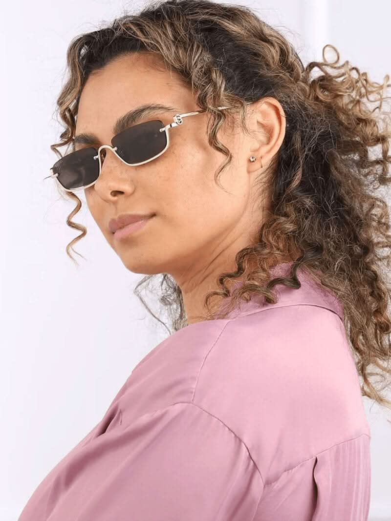 A woman wearing sleek rectangular gold-finish sunglasses on a bright city day.