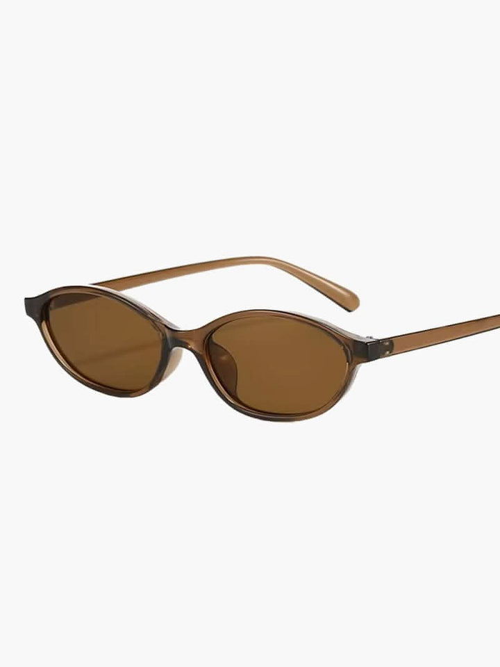 A woman by the sea wearing classic oval vintage sunglasses, relaxed and elegant in the sun.