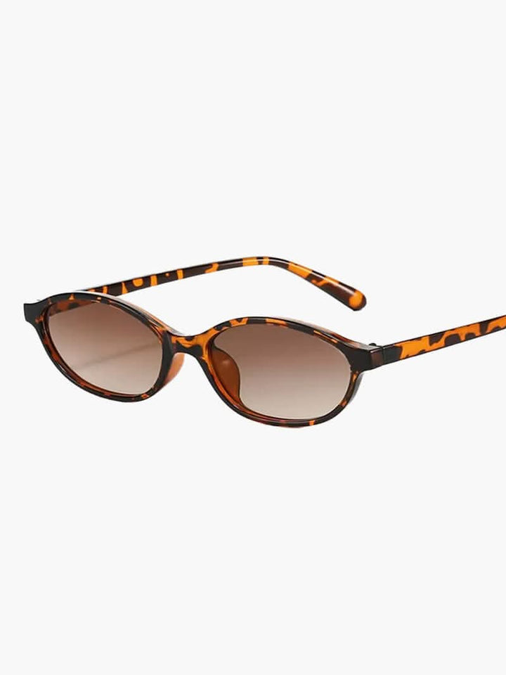 A woman by the sea wearing classic oval vintage sunglasses, relaxed and elegant in the sun.