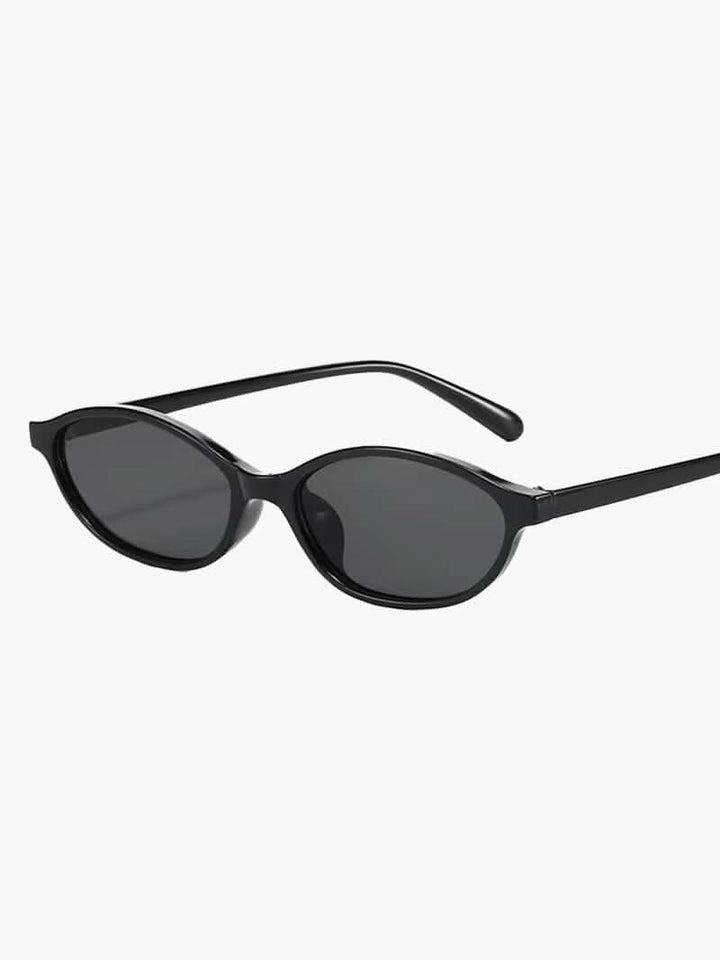 A woman by the sea wearing classic oval vintage sunglasses, relaxed and elegant in the sun.