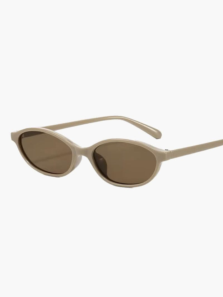 A woman by the sea wearing classic oval vintage sunglasses, relaxed and elegant in the sun.