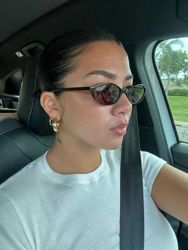 A woman by the sea wearing classic oval vintage sunglasses, relaxed and elegant in the sun.