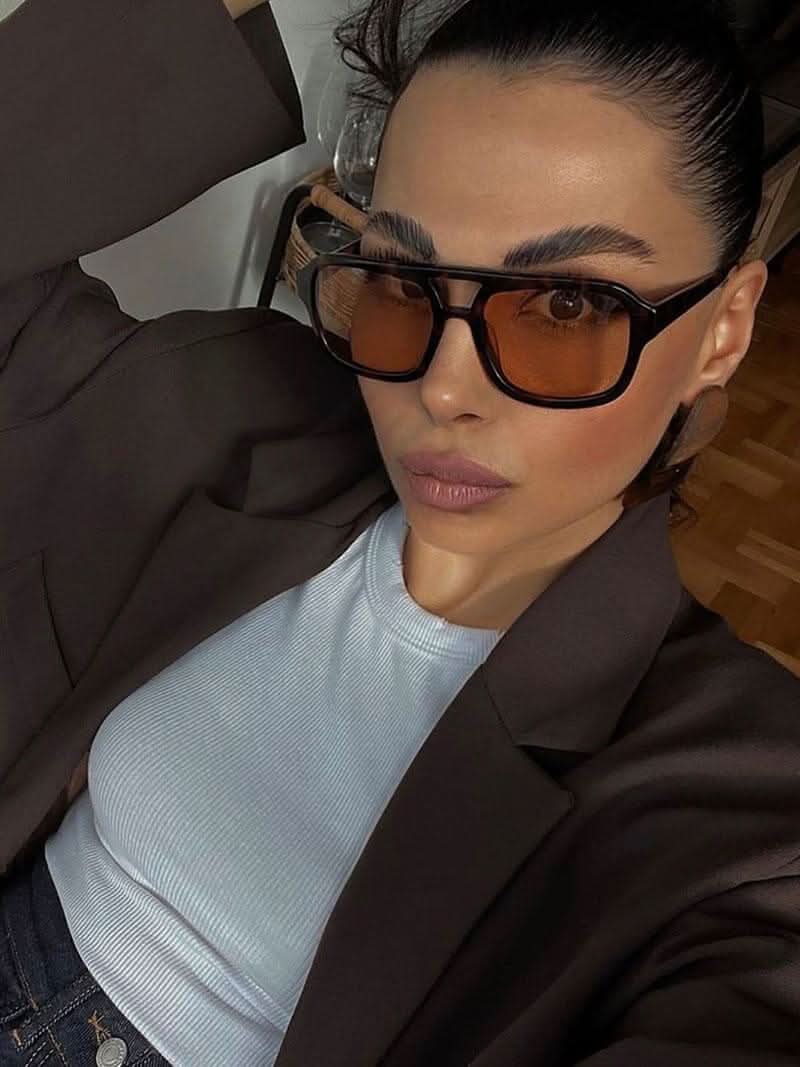 A woman wearing oversized tortoiseshell aviator sunglasses with green-tinted lenses on a sunny day outdoors.