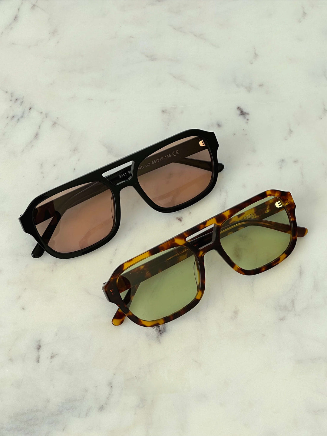 A woman wearing oversized tortoiseshell aviator sunglasses with green-tinted lenses on a sunny day outdoors.