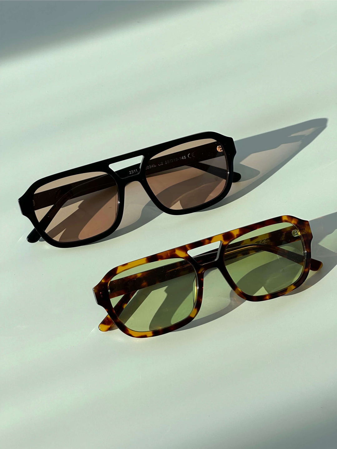 A woman wearing oversized tortoiseshell aviator sunglasses with green-tinted lenses on a sunny day outdoors.