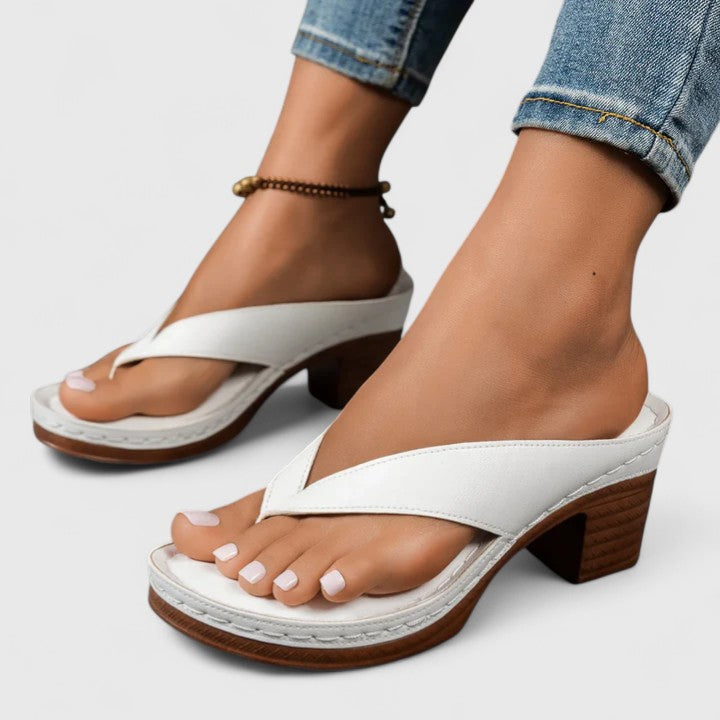 A woman in black open toe-post sandals with a chunky squared heel, walking easily through an evening event.