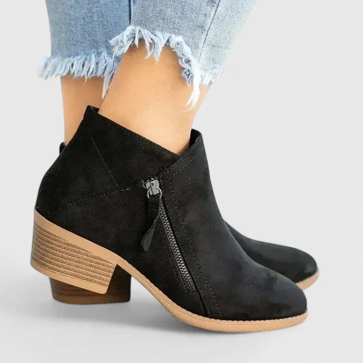 Woman wearing black side-zip ankle boots, stepping off a kerb in town.