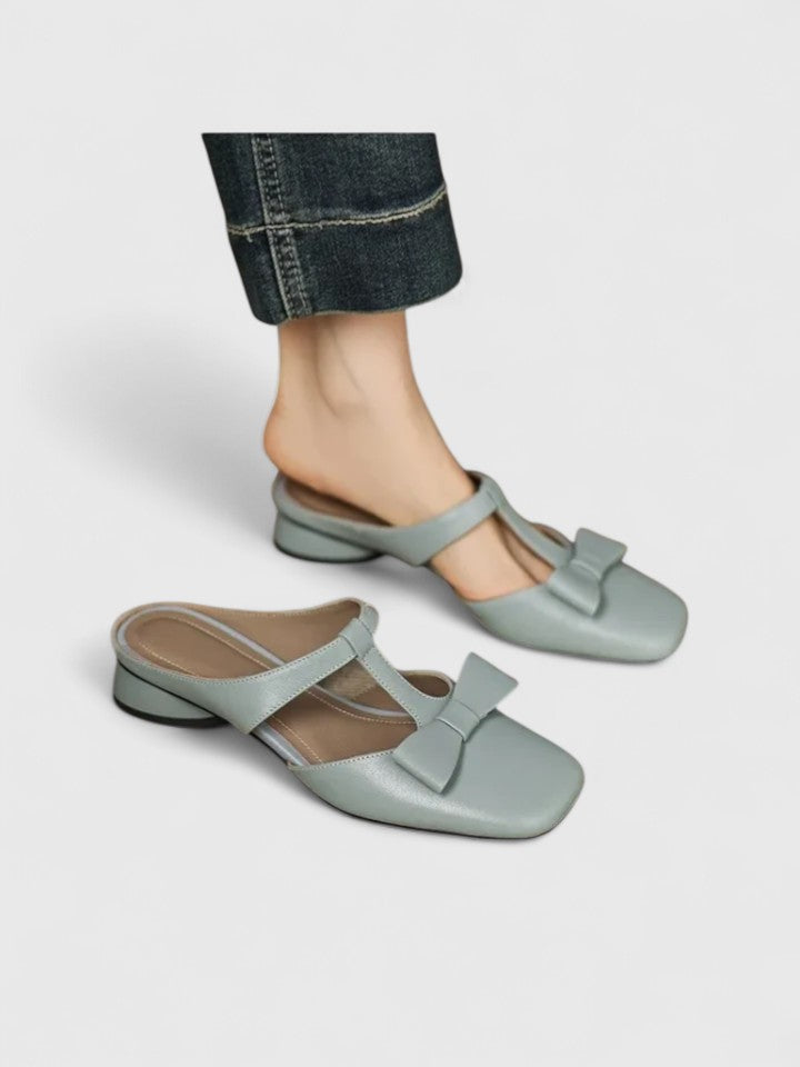 Soft green bow-detail mules with a slim T-strap, open back and a low heel.