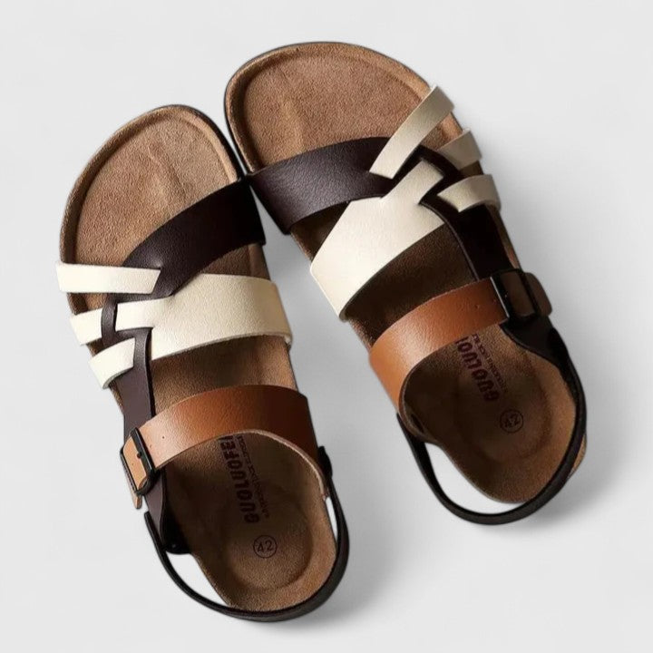 A woman wearing cream and brown multi-strap supportive sandals, standing steady and relaxed on a sunny path.