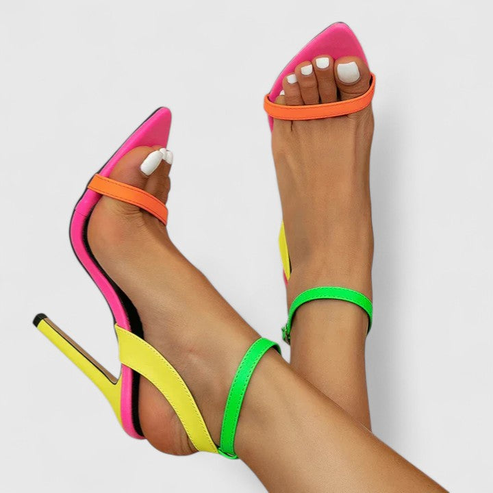 A woman wearing bright neon multicolour stiletto pumps with a slim heel and ankle strap.