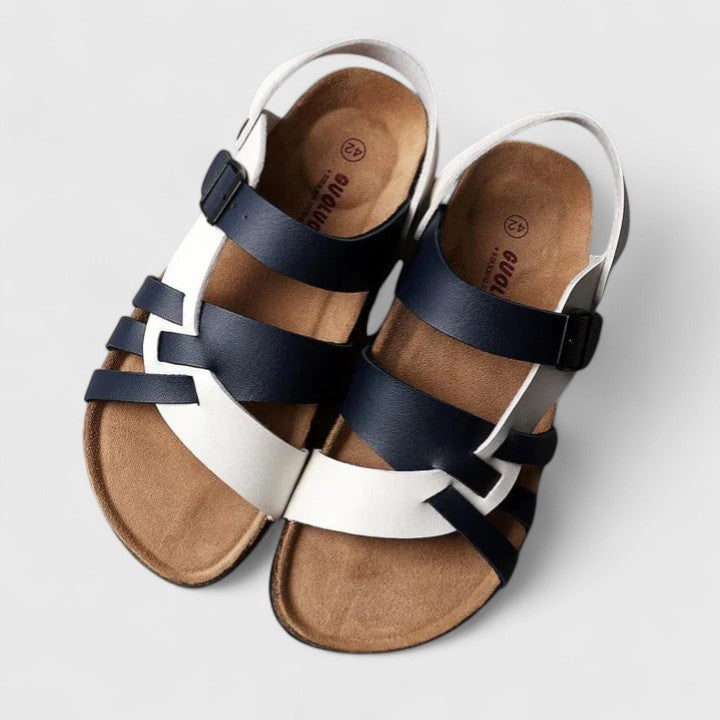 A woman wearing cream and brown multi-strap supportive sandals, standing steady and relaxed on a sunny path.