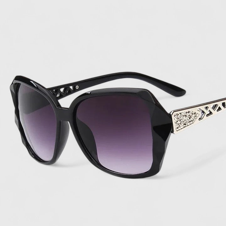 A woman on a sunny city street wearing chic square-frame sunglasses, smiling confidently.