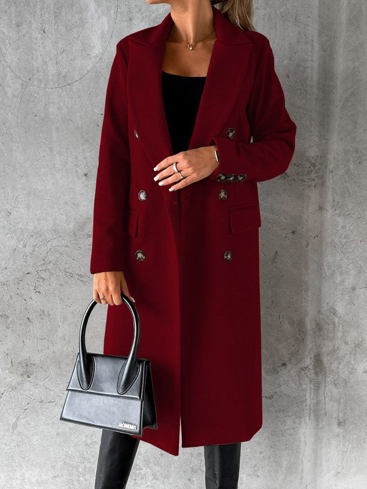 A woman wearing a long waisted coat, standing elegantly outdoors