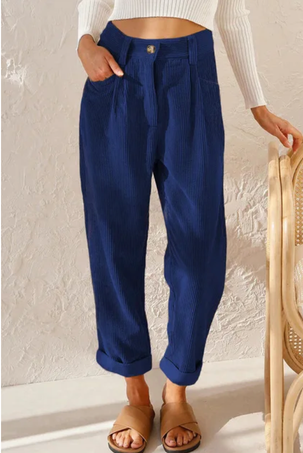Woman wearing loose high-waisted pants with a tucked-in top, standing in soft light.