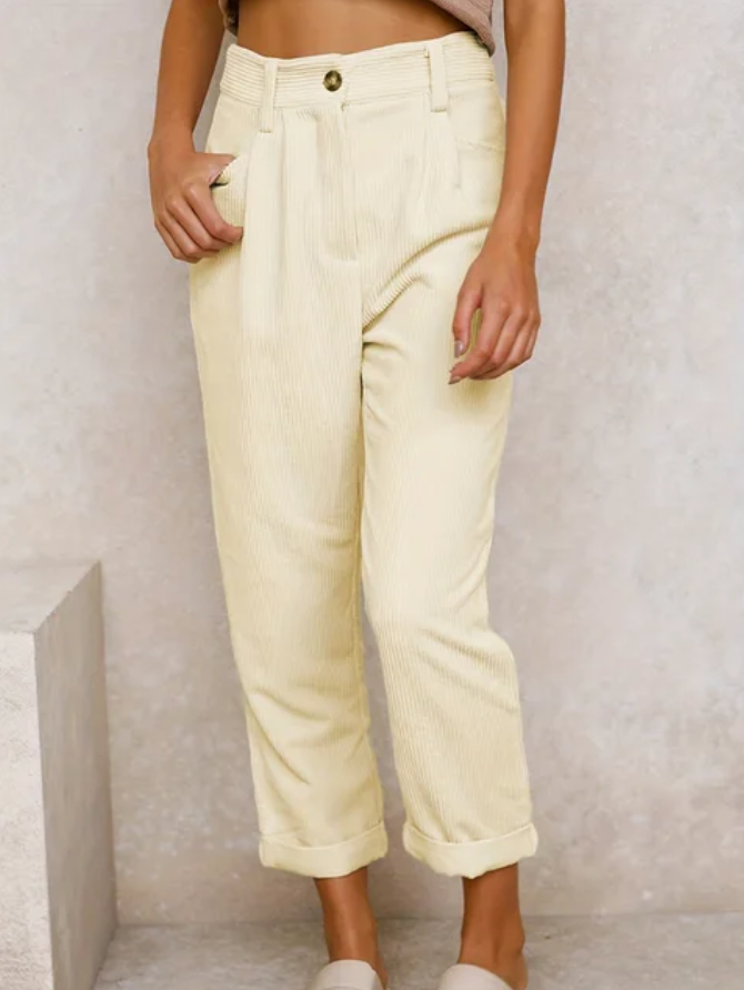 Woman wearing loose high-waisted pants with a tucked-in top, standing in soft light.