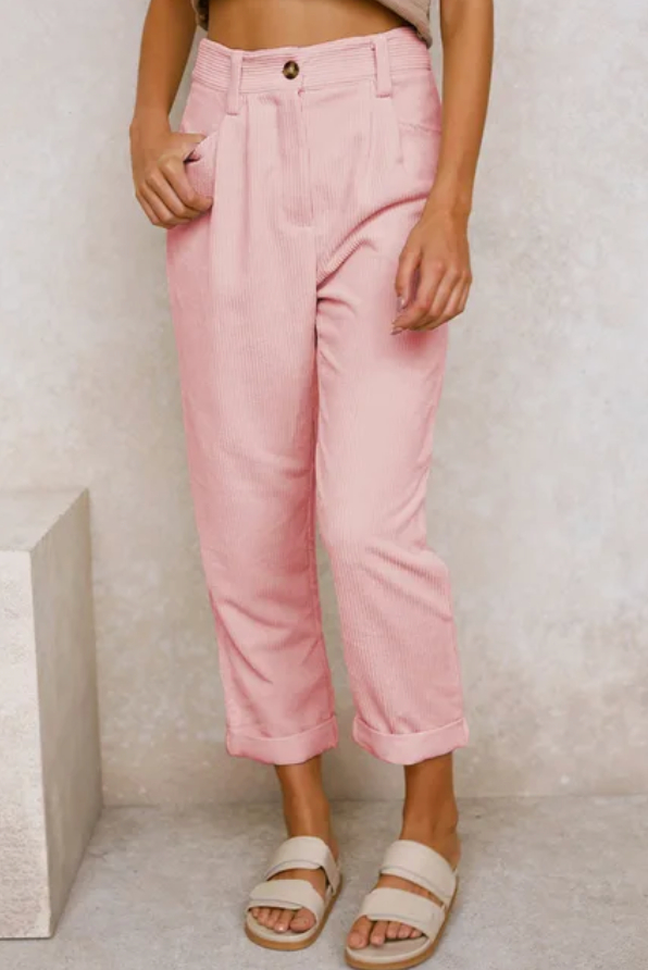 Woman wearing loose high-waisted pants with a tucked-in top, standing in soft light.