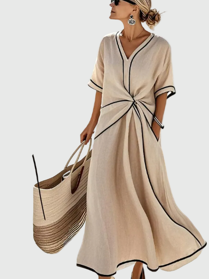Woman wearing a long flowing maxi dress with an elegant draped detail, standing in warm sunlight.