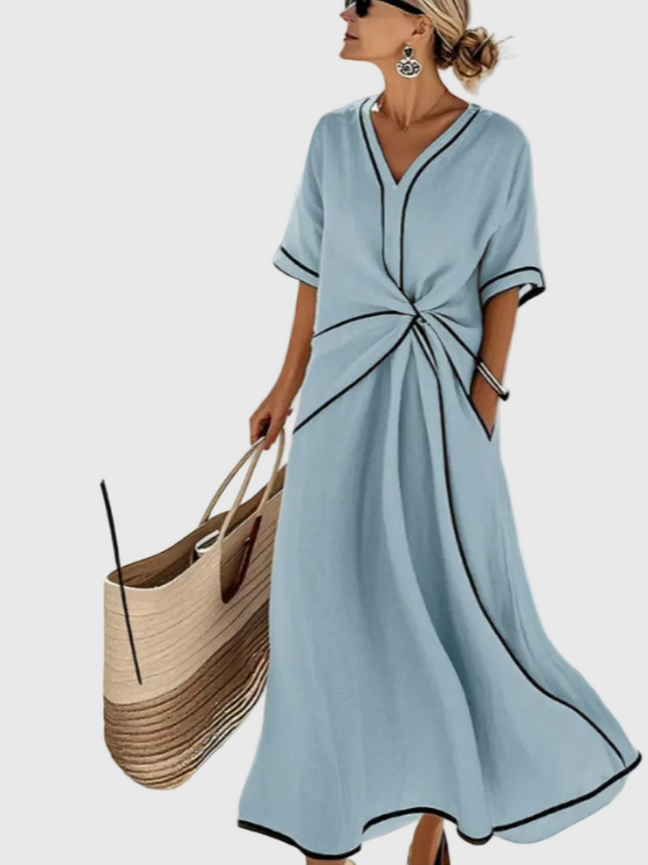 Woman wearing a long flowing maxi dress with an elegant draped detail, standing in warm sunlight.