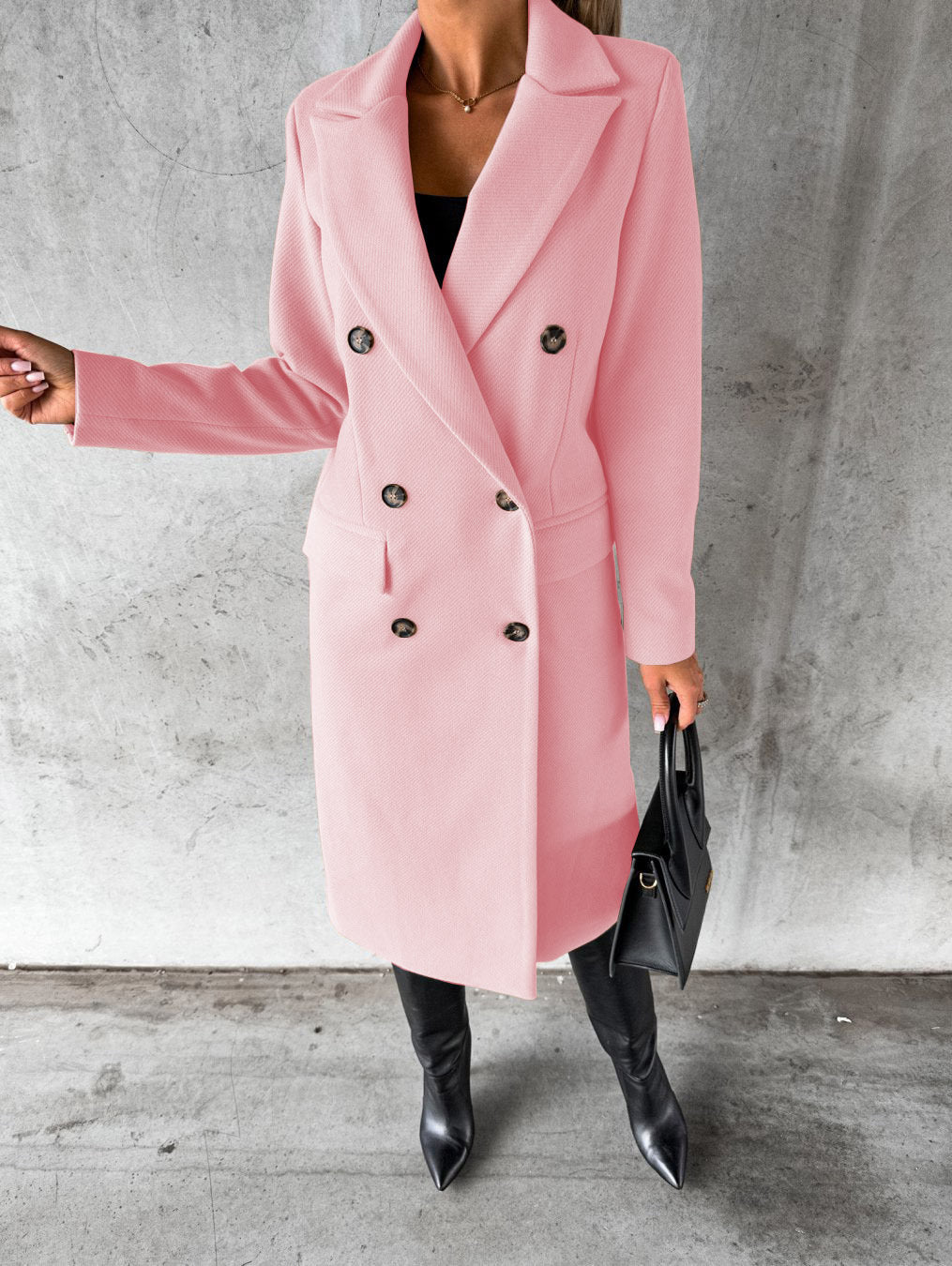 A woman wearing a long waisted coat, standing elegantly outdoors