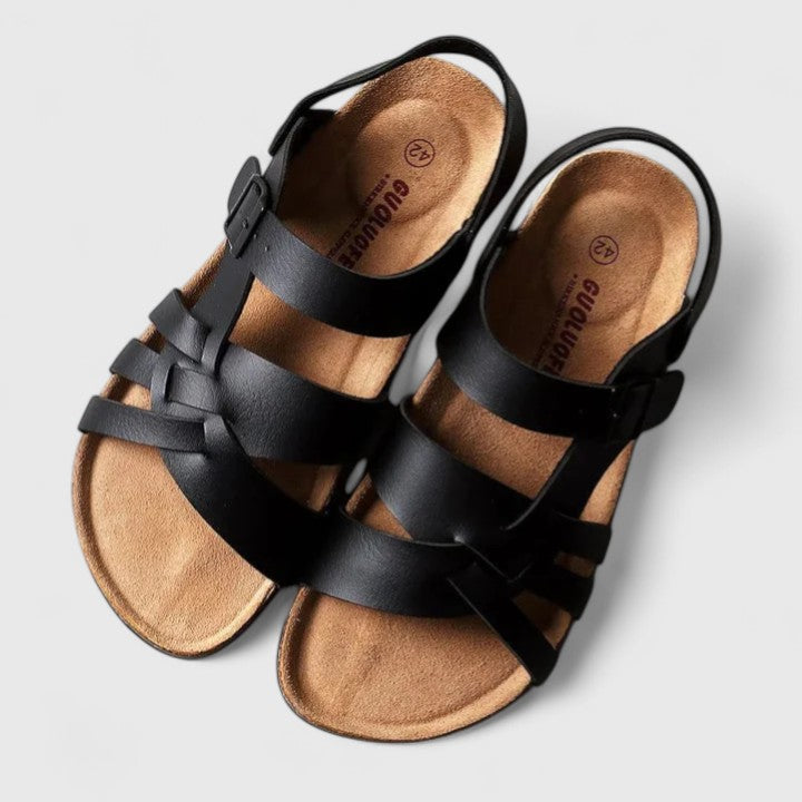 A woman wearing cream and brown multi-strap supportive sandals, standing steady and relaxed on a sunny path.