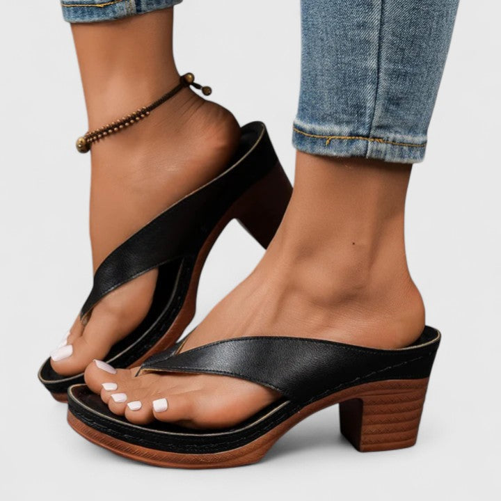 A woman in black open toe-post sandals with a chunky squared heel, walking easily through an evening event.