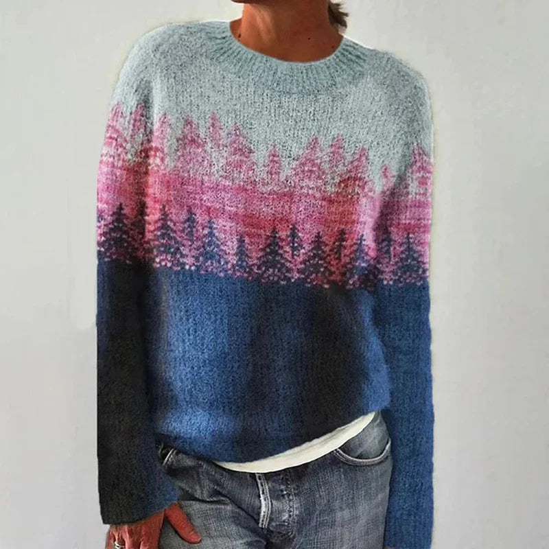 A woman wearing a sweater with a painterly pine forest print in pink, blue and grey, cosy and relaxed for fall.